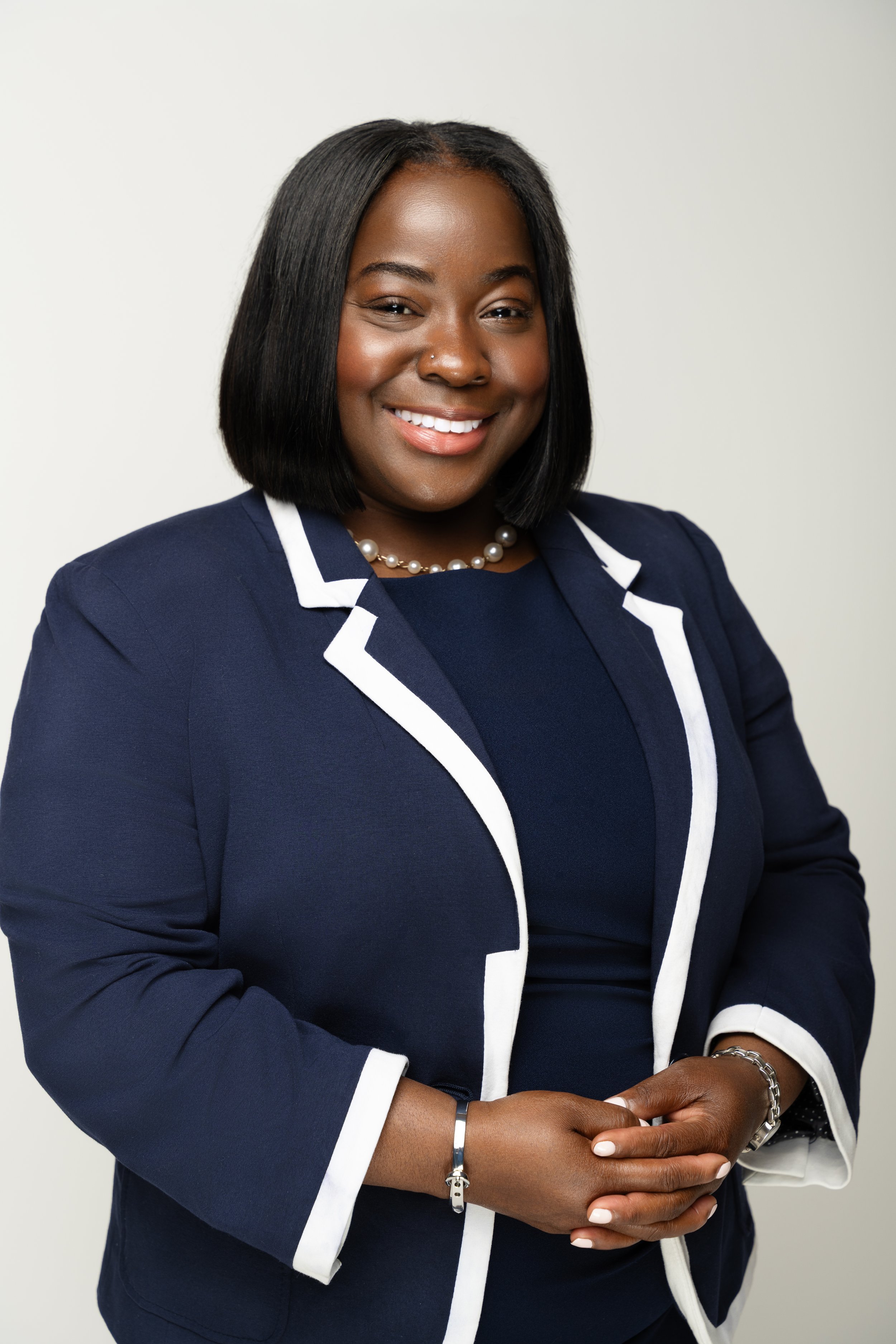 Adrienne McFarland, candidate for Chicago's 6th Ward Alderwoman, smiling in a navy blazer with white trim and a pearl necklace.