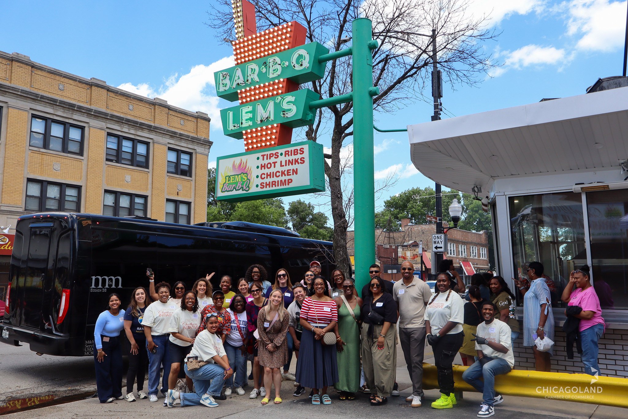 A large group of smiling residents and community leaders gathered outside Lem's Bar-B-Q on a 6th Ward street.
